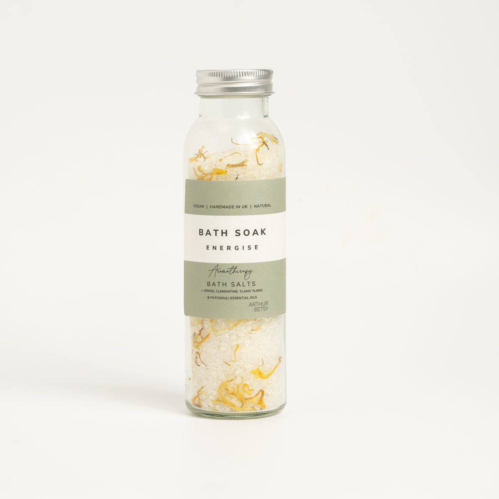 A glass bottle containing bath salts with textured recylable labels, labeled 'BATH SALTS energise'. self care gifts