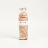 A glass bottle containing bath salts with a label that reads 'BATH SOAK FOCUS'. The background is white and clean. Wellbeing gifts
