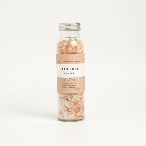 A glass bottle containing bath salts with a label that reads 'BATH SOAK FOCUS'. The background is white and clean. Wellbeing gifts