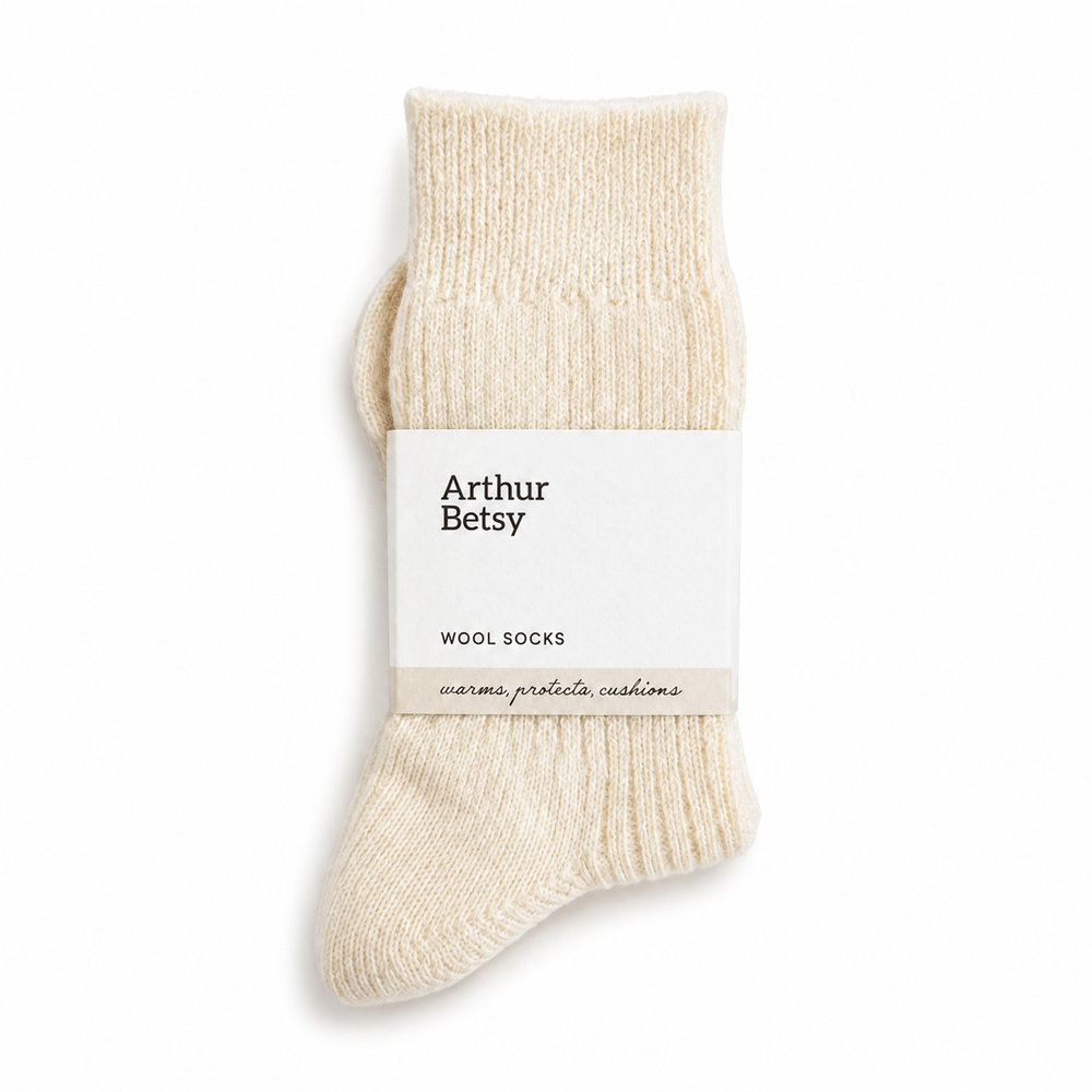 A single cream-colored knit wool sock with a white paper band label reading 'Arthur Betsy WOOL SOCKS' on a clean white background. Arthur Betsy luxury wool-blend socks in Cold Cream, designed for softness, warmth and comfortable everyday wear.