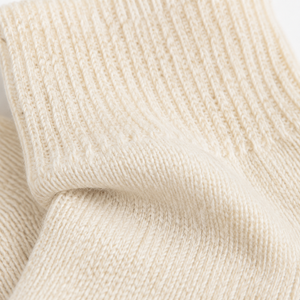 Close-up of a cream-colored ribbed knit fabric, showing the detailed texture and folds of the material. Cold Cream wool-blend socks in a versatile one-size fit, perfect for cosy lounging, relaxing evenings and colder days.