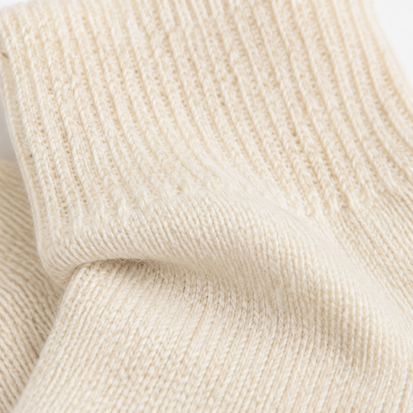 Close-up of a cream-colored ribbed knit fabric, showing the detailed texture and folds of the material. Cold Cream wool-blend socks in a versatile one-size fit, perfect for cosy lounging, relaxing evenings and colder days.
