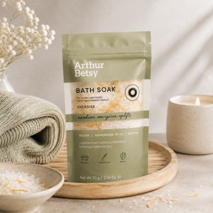 Arthur Betsy Energise Bath Soak in a sage green stand-up pouch, styled on a wooden tray with a folded sage-green towel, a ceramic candle, and a bowl of bath salts. Uplifting single-bath salt sachet with citrus, floral and earthy botanical notes—ideal for travelling, pampering or gifting.