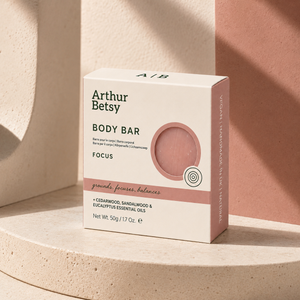 Arthur Betsy Focus Body Bar box in a soft cream color with dusty pink accents, displayed on a beige stone pedestal with a terracotta background. Artisan body soap made in Staffordshire with plant-based oils, moisturising glycerin and pure essential oils, presented in minimal recyclable packaging.
