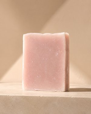 A single rectangular bar of pale pink soap standing upright on a beige stone-like surface against a warm beige background with soft diagonal shadows. Staffordshire-made cedarwood, sandalwood and eucalyptus soap in minimal recyclable packaging—a thoughtful birthday, Christmas or self-care gift.