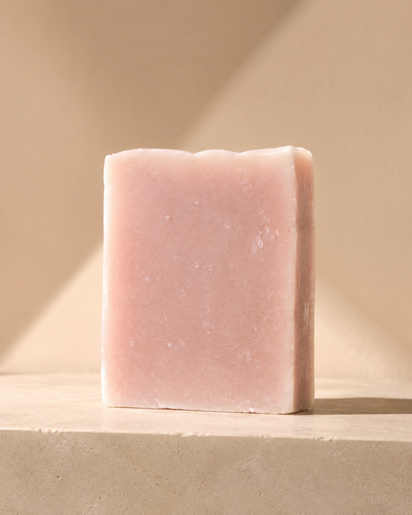 A single rectangular bar of pale pink soap standing upright on a beige stone-like surface against a warm beige background with soft diagonal shadows. Staffordshire-made cedarwood, sandalwood and eucalyptus soap in minimal recyclable packaging—a thoughtful birthday, Christmas or self-care gift.