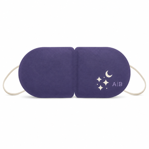 A purple sleep mask with white elastic ear loops and a white crescent moon and star graphic on the right side, shown on a plain white background. Unscented warming eye mask that activates when opened, offering calming heat for relaxation, bedtime, travel or flights.