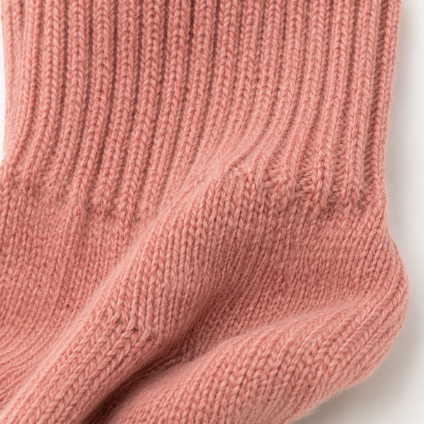 A close-up of a ribbed knit sock in a dusty rose pink color, showing the detailed texture of the yarn and stitching. Soft pink wool socks made from alpaca wool, nylon and spandex—a luxurious winter accessory and thoughtful self-care gift.