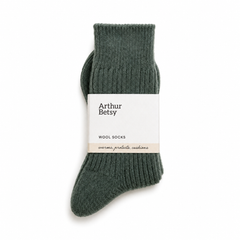 A pair of ribbed knit wool socks in a muted dark green, wrapped with a white paper band labeled 'Arthur Betsy'. Arthur Betsy luxury alpaca wool socks in Nordic Pine green, made with an 80% alpaca wool blend for warmth, softness and everyday comfort.