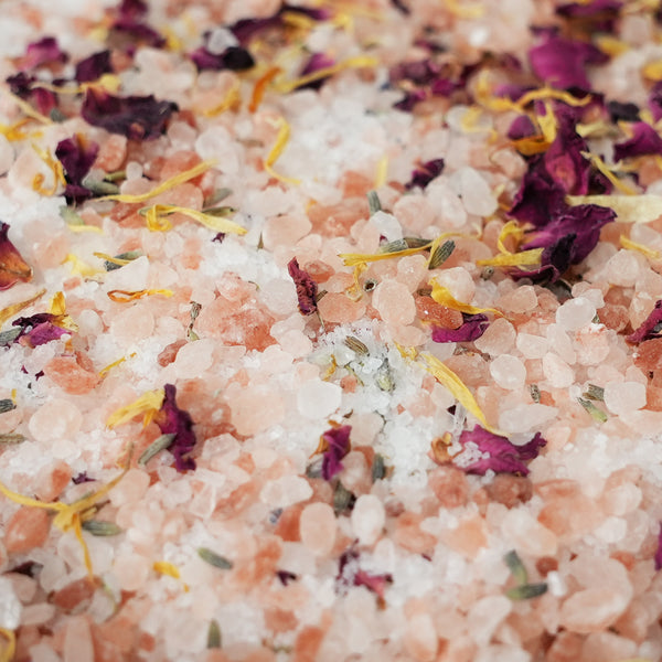 Close-up of pink Himalayan salt crystals mixed with dried purple rose petals and yellow flower petals.