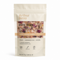 A stand-up pouch of Arthur Betsy Bath Soak in the Restore scent, featuring a cream-colored package with a clear window showing pink and purple bath salts inside. Calming single-bath salt sachet with soothing lavender, herbal rosemary and warming cardamom notes, perfect for travelling, pampering or wellbeing gifting.