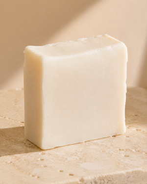 A single rectangular bar of creamy off-white soap standing upright on a textured beige stone surface with a soft beige background. Natural lavender soap bar with nourishing olive oil, coconut oil, shea butter, castor oil and sweet almond oil for gentle everyday cleansing.