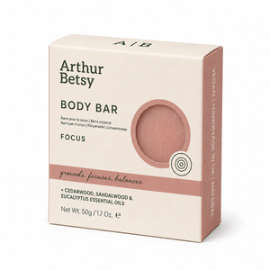 Arthur Betsy Focus Body Bar box packaging, featuring a cream-colored box with dusty rose accents and a circular cutout showing the pinkish-rose bar inside. Arthur Betsy 50g handmade body soap with cedarwood, sandalwood and eucalyptus essential oils, hand-poured in Staffordshire using the traditional cold-process method.