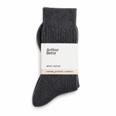 A pair of dark charcoal gray ribbed wool socks with a white paper band label that reads 'Arthur Betsy WOOL SOCKS', shown on a clean white background. Arthur Betsy luxury alpaca wool socks in Twilight blue, made with an 80% alpaca wool blend for warmth, softness and everyday comfort.
