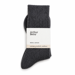A pair of dark charcoal gray ribbed wool socks with a white paper band label that reads 'Arthur Betsy WOOL SOCKS', shown on a clean white background. Arthur Betsy luxury alpaca wool socks in Twilight blue, made with an 80% alpaca wool blend for warmth, softness and everyday comfort.