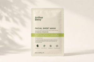 Arthur Betsy Intensive Hydration Facial Sheet Mask in a 25ml single-use stand-up pouch, displayed against a warm off-white background with soft leaf shadows. Paraben-free facial sheet mask enriched with sodium hyaluronate, plant extracts, peptides and gold for an at-home spa skincare treatment.