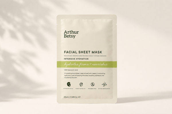 Arthur Betsy Intensive Hydration Facial Sheet Mask in a 25ml single-use stand-up pouch, displayed against a warm off-white background with soft leaf shadows. Paraben-free facial sheet mask enriched with sodium hyaluronate, plant extracts, peptides and gold for an at-home spa skincare treatment.