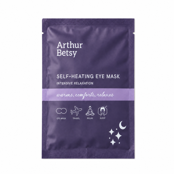 Arthur Betsy Self-Heating Eye Mask in a dark purple stand-up pouch with white text and a light purple horizontal band across the center, shown on a plain white background. Arthur Betsy self-heating eye mask providing around 20 minutes of gentle, soothing warmth to relax tired eyes and encourage rest.