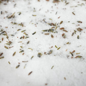 Close-up of coarse white salt crystals scattered with small dried green and brown herb seeds on top. Relaxing aromatherapy bath soak with lavender, peppermint, eucalyptus and rosemary essential oils, designed for a calming evening self-care ritual.